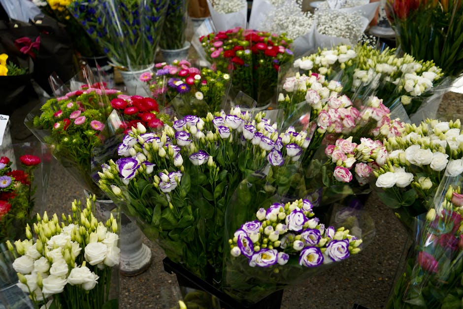 A vibrant display of fresh floral bouquets arranged with a variety of flowers including white, purple, pink, and red blossoms, each wrapped in clear plastic and placed on a dark stone surface at flori